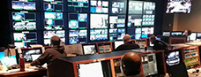 television production control room with a wall of video monitors and people watching them.